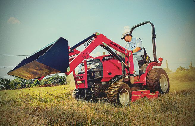 Technician checking engine oil and fluid levels on a Mahindra tractor